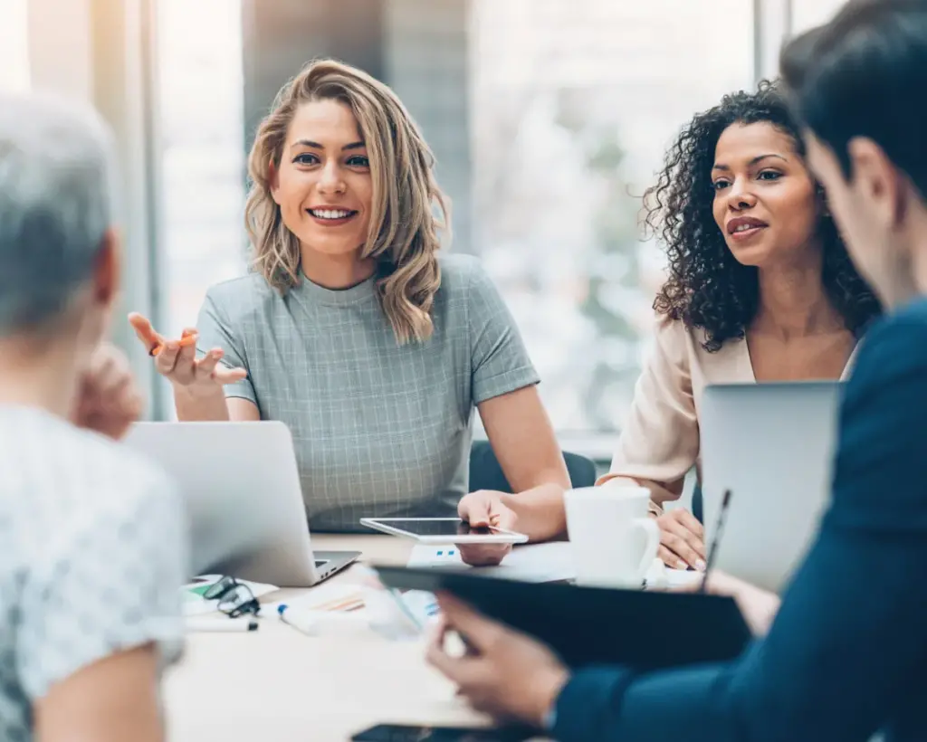 Two female identifying people in business dress talking to two other people in an office setting.